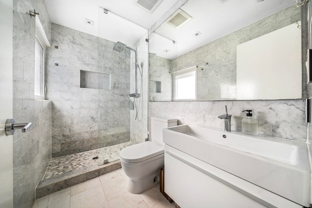 bathroom with a tile shower, vanity, tile walls, and toilet