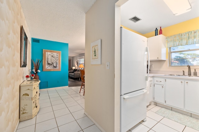 kitchen with sink, white cabinets, white refrigerator, a textured ceiling, and light tile patterned floors