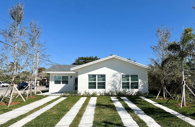 view of front facade with roof with shingles, a front yard, and stucco siding