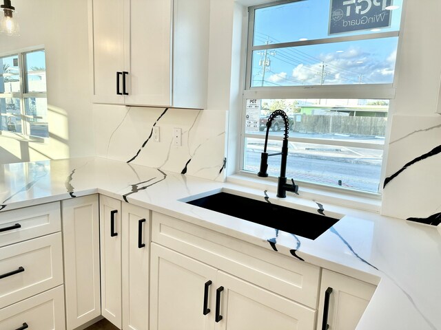 kitchen featuring decorative backsplash, light wood-type flooring, light stone counters, pendant lighting, and white cabinets