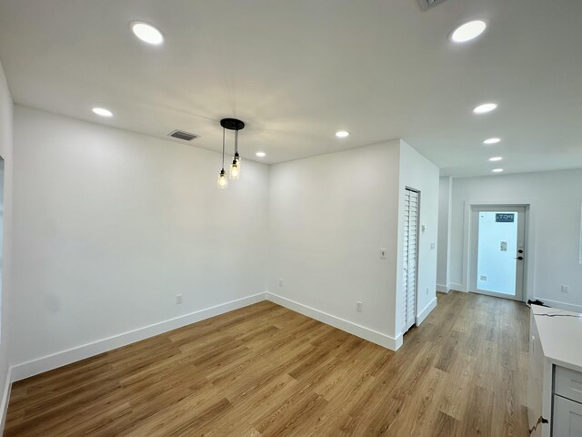 kitchen featuring kitchen peninsula, light wood-type flooring, backsplash, decorative light fixtures, and white cabinets