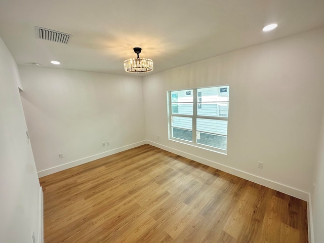 spare room featuring light wood-type flooring and a chandelier