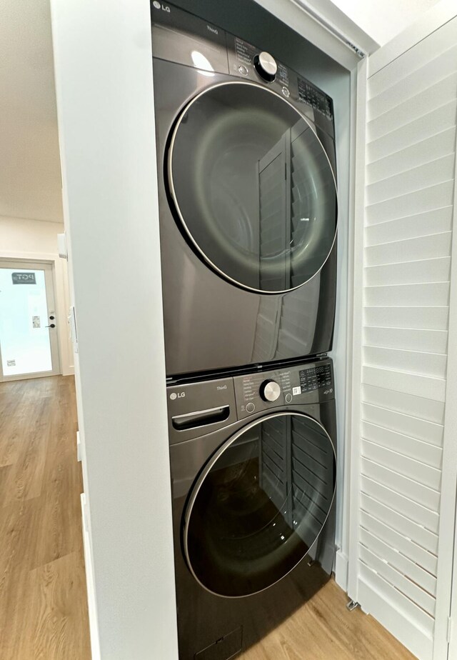 clothes washing area featuring stacked washer / dryer, laundry area, and wood finished floors