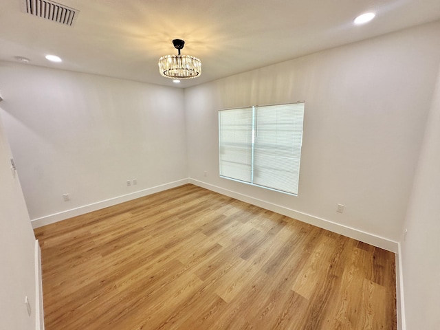 empty room featuring a notable chandelier, light wood finished floors, recessed lighting, visible vents, and baseboards