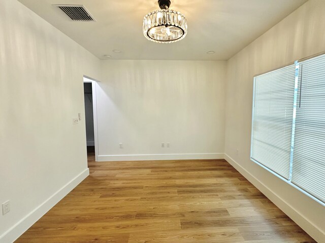 unfurnished room featuring baseboards, light wood-style floors, visible vents, and an inviting chandelier