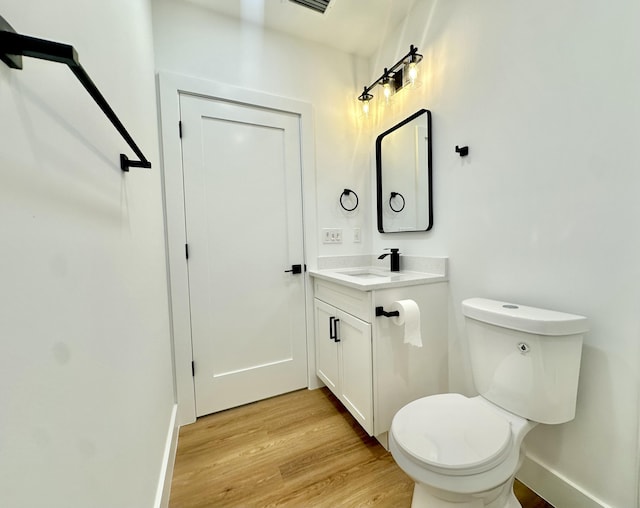 half bathroom with toilet, wood finished floors, vanity, and baseboards