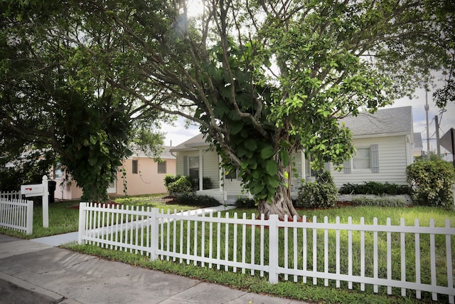 view of property hidden behind natural elements featuring a fenced front yard and a front lawn