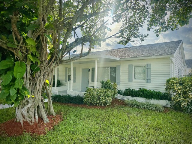 view of front of house featuring covered porch, a shingled roof, and a front yard