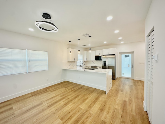 kitchen featuring light wood finished floors, tasteful backsplash, a peninsula, stainless steel appliances, and light countertops