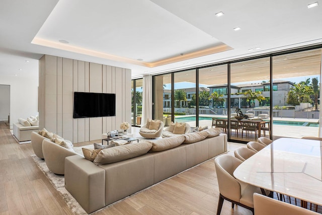 living room featuring a raised ceiling, a wall of windows, and light hardwood / wood-style flooring