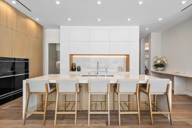 kitchen featuring a kitchen breakfast bar, sink, a large island with sink, light hardwood / wood-style flooring, and white cabinets