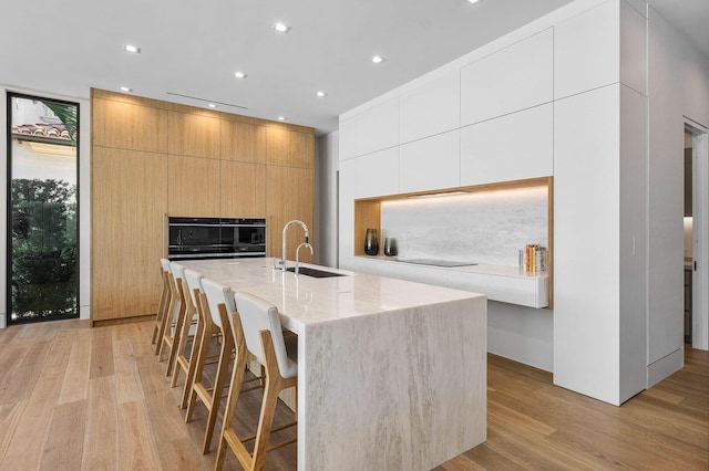 kitchen with sink, an island with sink, light hardwood / wood-style floors, a kitchen bar, and white cabinets