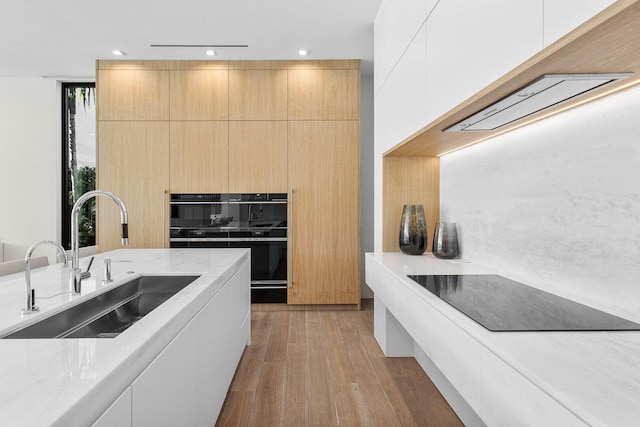 kitchen featuring sink, light hardwood / wood-style flooring, light stone countertops, double oven, and white cabinetry