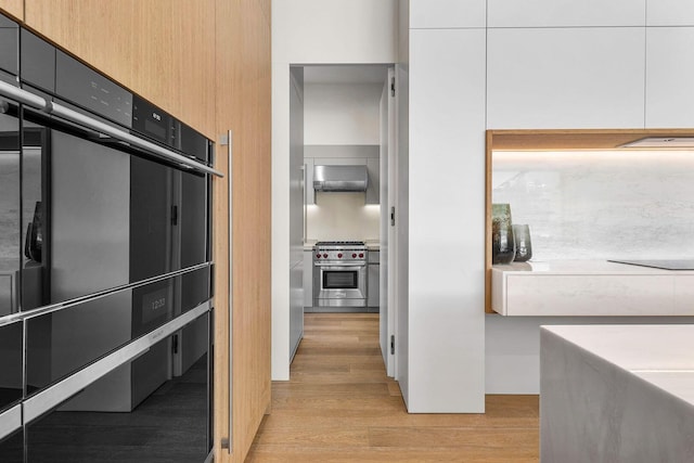 kitchen featuring white cabinetry, luxury range, wall chimney range hood, and light hardwood / wood-style floors