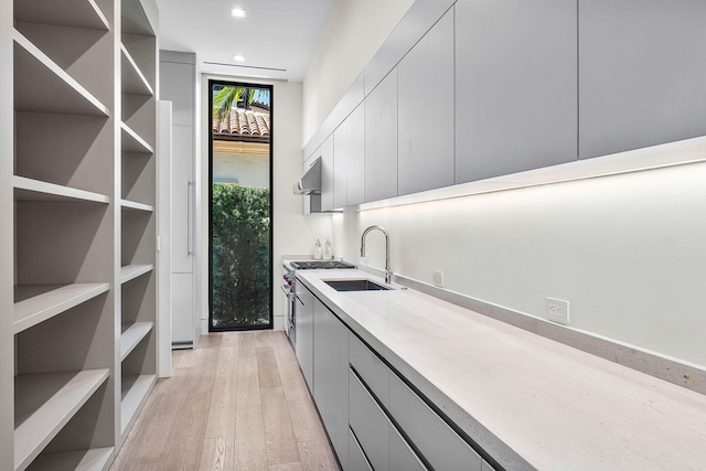 bar featuring range hood, gray cabinets, light hardwood / wood-style flooring, and sink