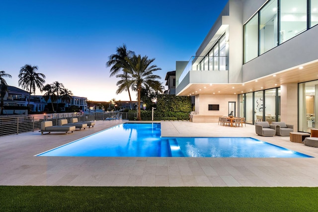 pool at dusk with a patio area and an outdoor fireplace