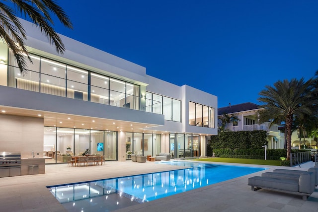 pool at night with an outdoor kitchen, a grill, and a patio area