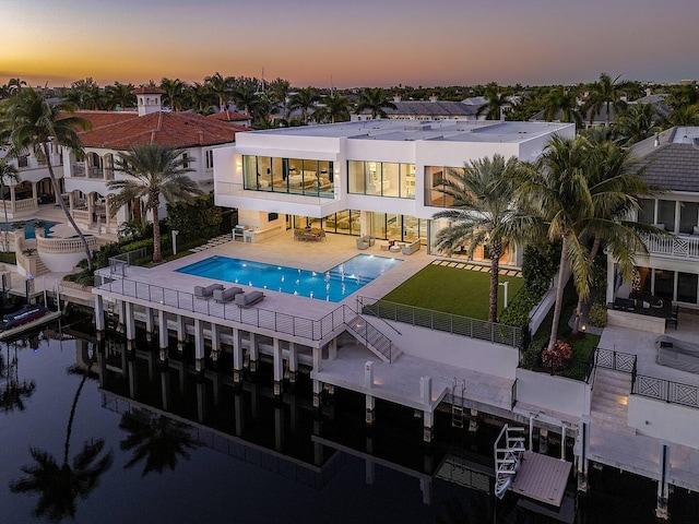 224 W Key Palm Rd, Boca Raton, FL 33432 - back of house at dusk with a balcony, a fenced backyard, a patio, an outdoor pool, and a water view