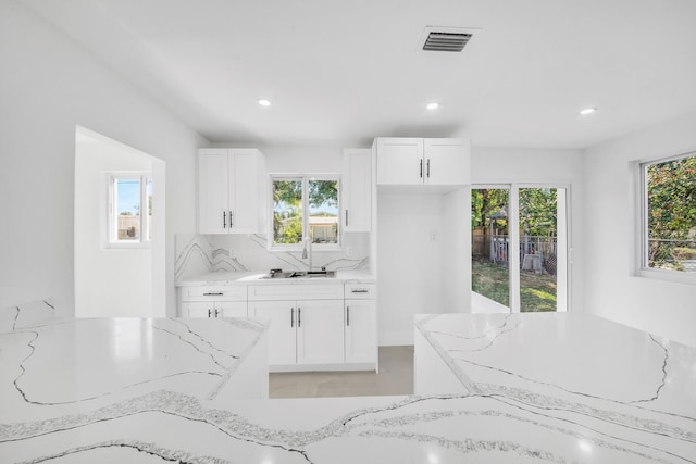 kitchen with light stone counters, visible vents, white cabinetry, and tasteful backsplash