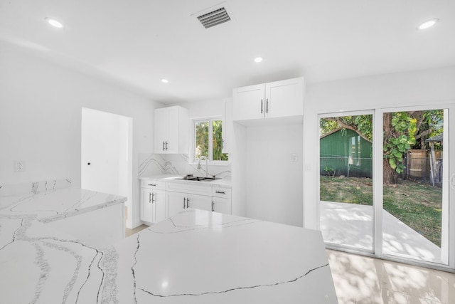 kitchen featuring visible vents, backsplash, light stone counters, white cabinetry, and a sink