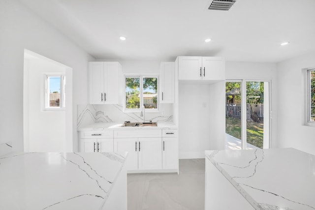 kitchen with visible vents, backsplash, light stone countertops, white cabinets, and a sink