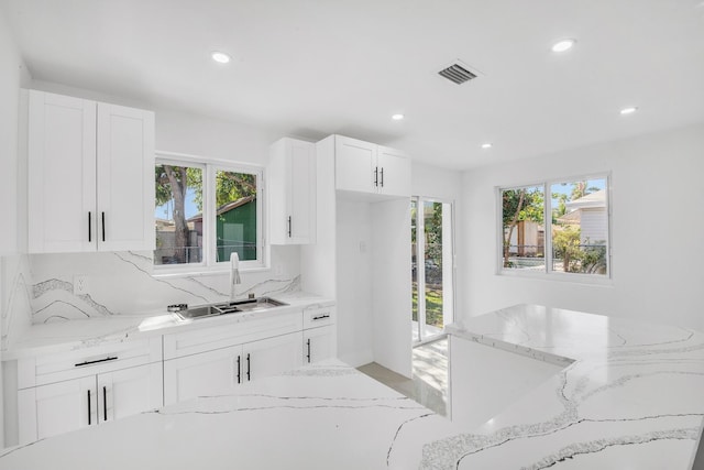 kitchen with white cabinetry, light stone countertops, visible vents, and a sink