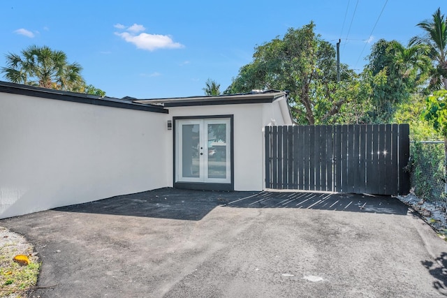 doorway to property featuring french doors, fence, uncovered parking, and stucco siding