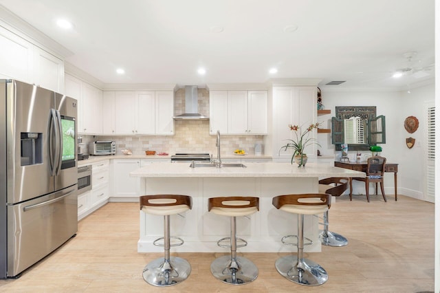 kitchen with white cabinetry, sink, wall chimney exhaust hood, stainless steel appliances, and a center island with sink