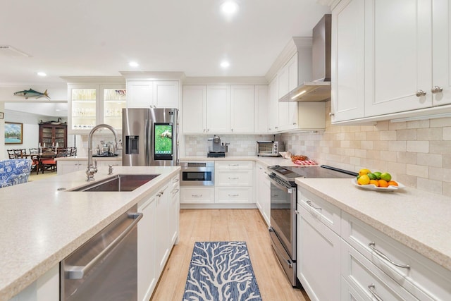 kitchen featuring white cabinetry, sink, wall chimney exhaust hood, appliances with stainless steel finishes, and light wood-type flooring