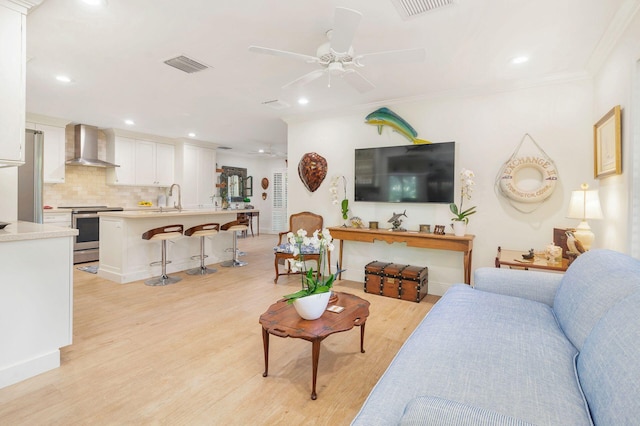 living room with ceiling fan, light wood-type flooring, sink, and ornamental molding