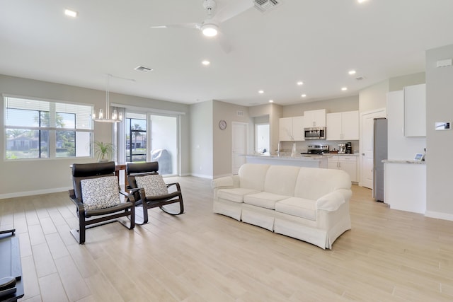 living room with ceiling fan with notable chandelier and light wood-type flooring