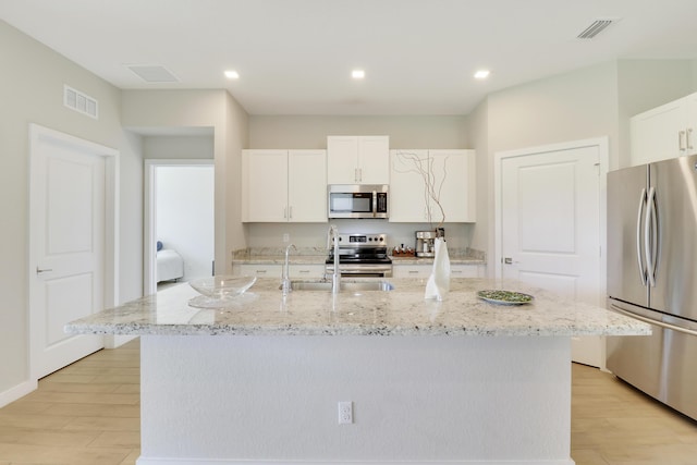 kitchen with stainless steel appliances, white cabinetry, a center island with sink, and light hardwood / wood-style floors