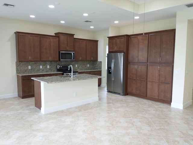 kitchen with a kitchen island with sink, light stone countertops, tasteful backsplash, dark brown cabinetry, and stainless steel appliances