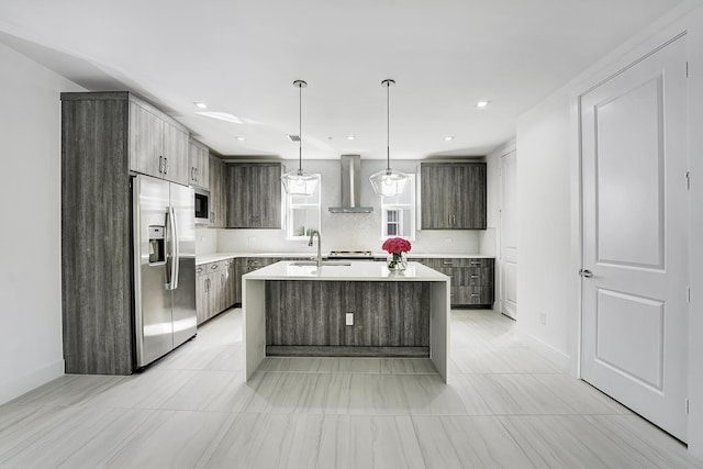 kitchen featuring dark brown cabinetry, stainless steel appliances, sink, wall chimney range hood, and a center island with sink