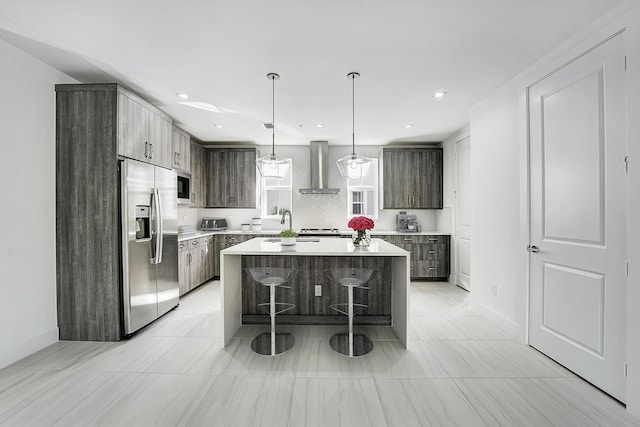 kitchen with a kitchen breakfast bar, wall chimney range hood, a kitchen island, dark brown cabinetry, and stainless steel appliances