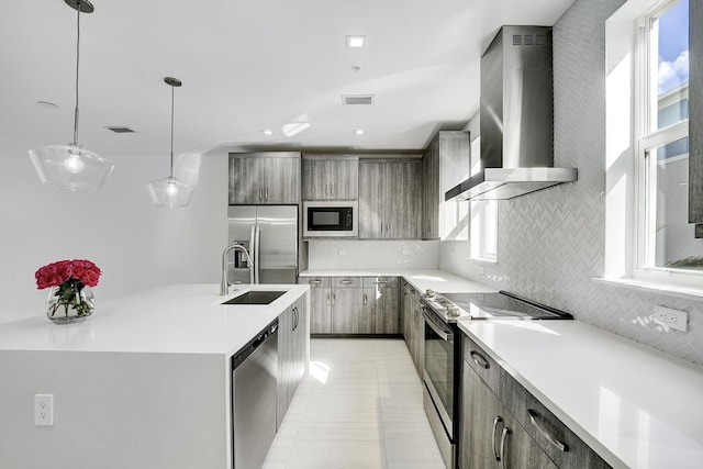 kitchen featuring decorative light fixtures, sink, stainless steel appliances, and wall chimney range hood