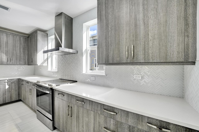 kitchen with gray cabinets, wall chimney exhaust hood, light tile patterned floors, and stainless steel range with electric cooktop