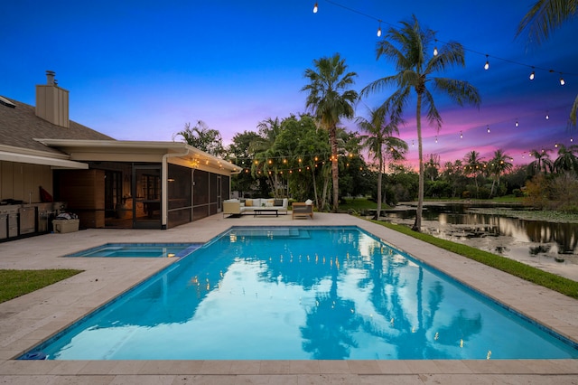 pool at dusk with an in ground hot tub, an outdoor living space, a water view, a patio area, and a sunroom