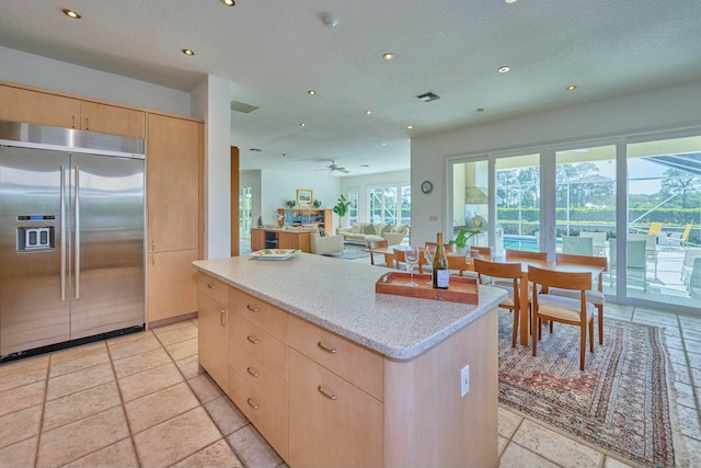 kitchen featuring ceiling fan, a center island, light stone countertops, light brown cabinets, and stainless steel built in fridge