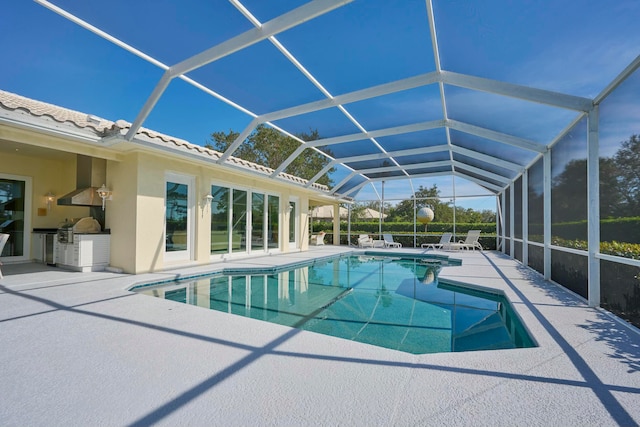 view of pool with a patio area, exterior kitchen, and glass enclosure