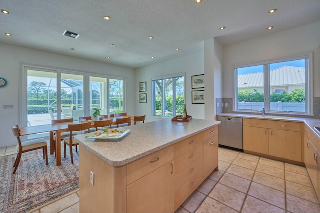 kitchen featuring dishwasher, a center island, a textured ceiling, and light brown cabinetry