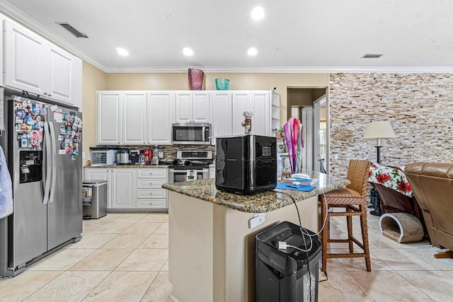 kitchen featuring appliances with stainless steel finishes, dark stone counters, a kitchen bar, white cabinets, and ornamental molding