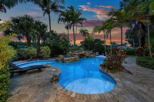 pool at dusk featuring an in ground hot tub and a patio