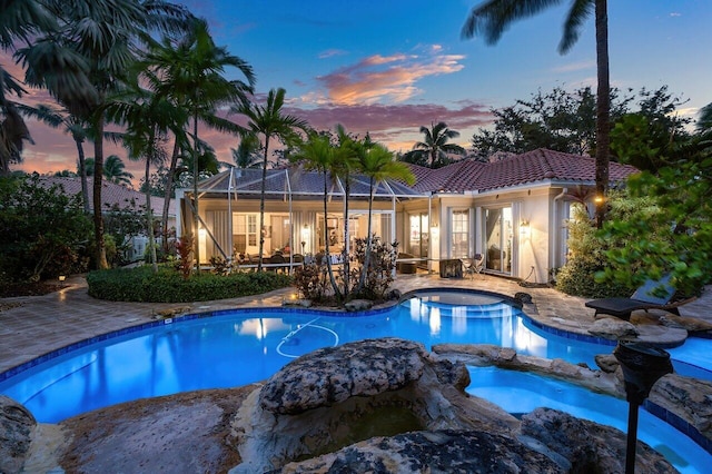 7580 Red River Rd, West Palm Beach, FL 33411 - pool at dusk with glass enclosure, a patio, and a pool with connected hot tub