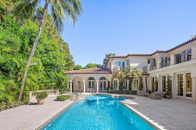 back of property featuring a balcony, a patio, french doors, and a swimming pool with hot tub