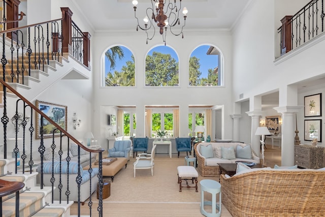 living room featuring a high ceiling, ornamental molding, a chandelier, and ornate columns