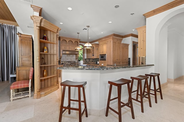 kitchen featuring kitchen peninsula, decorative backsplash, dark stone counters, stainless steel microwave, and pendant lighting