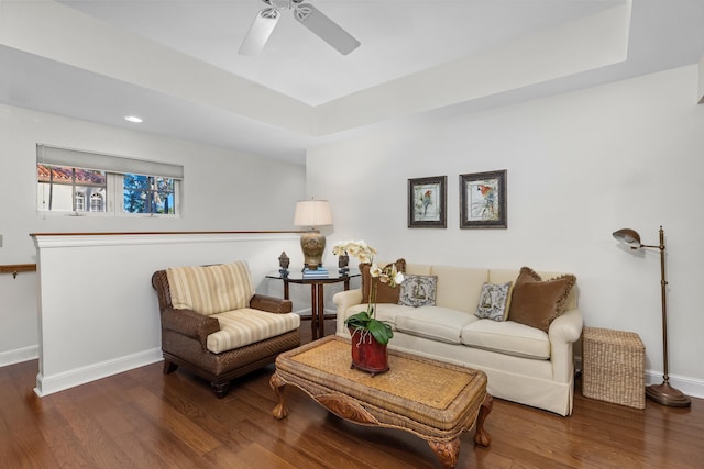 living room with ceiling fan, dark wood-type flooring, and a raised ceiling