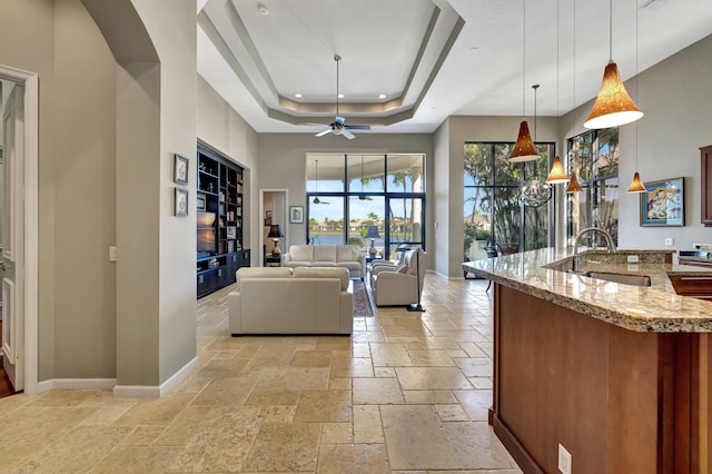 living room featuring a towering ceiling, a tray ceiling, ceiling fan, and sink