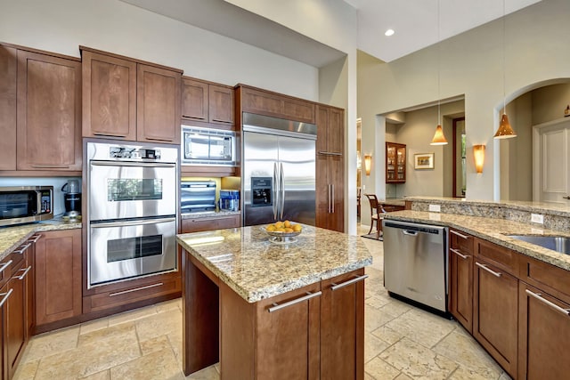 kitchen featuring light stone countertops, sink, built in appliances, pendant lighting, and a kitchen island